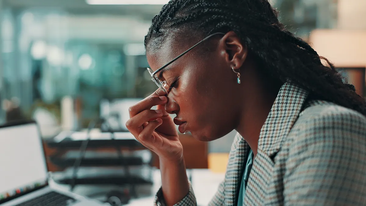 A woman experiencing a migraine and pinching the root of her nose