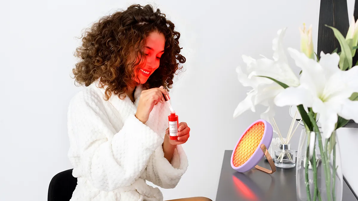 A woman using Lighthouse red light therapy panel and UFO red light serum
