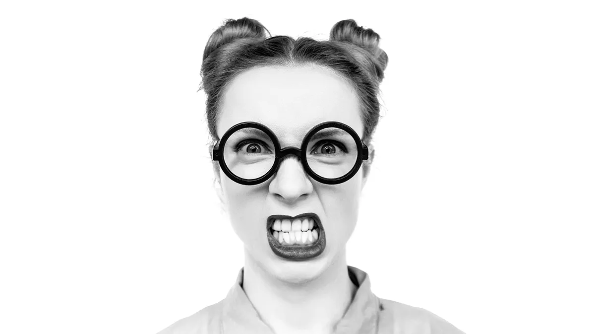 A woman with two hair buns, thick rim glasses and showing her perfectly white teeth with a growl