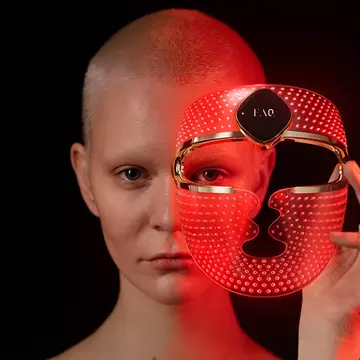 Androgynous beautiful young woman with short hair putting on FAQ 202 red light therapy mask