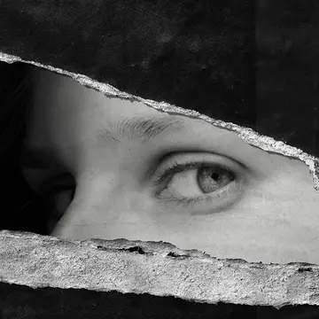 A torn up black and wihte poster on the wall where only a womans eyes remain, looking at the viewer