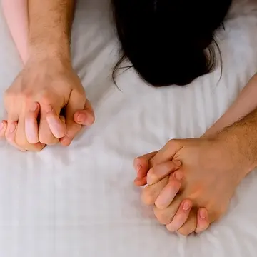 A couple clutching hands during sex on white sheets