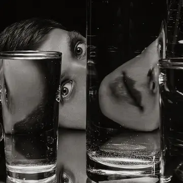 A person with interesting eyes with a face deconstructed by glasses of water in front of them