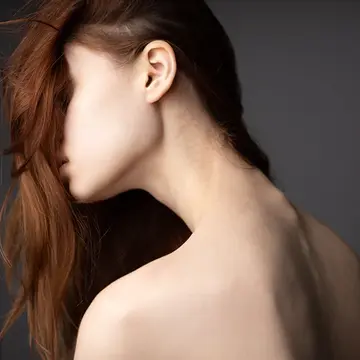 A woman with beautiful healthy hair falling over her face showing the slender and pale back of her neck