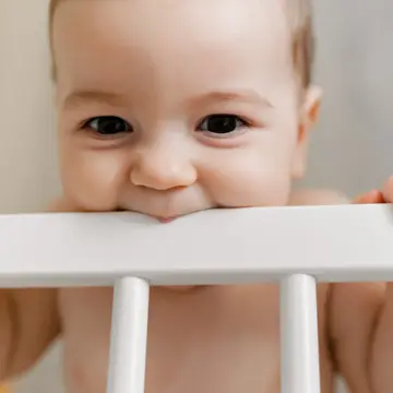 A cute teething baby chewing on the crib bar