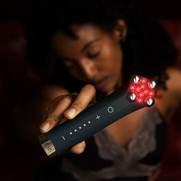 A blurry woman in the shadows holding FAQ 402 dual microcurrent and NIR facial toning device in a closeup main frame