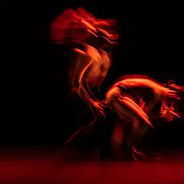 An abstract dance in a dark room with red lights representing the dualism and similarities of red light therapy vs infrared