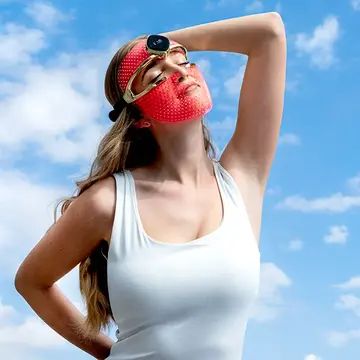 A young woman in a white top wearing FAQ 202 red LED light mask
