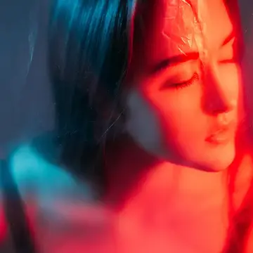 A woman behind a translucent barrier, eyes closed and illuminated by red light therapy