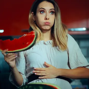A bloated woman eating a watermellon  
