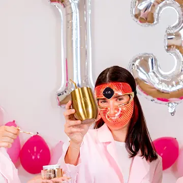 Three young women celebrating FOREO birthday sale with drinks and doing skincare in a white and pink setting