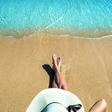 A woman in a white wide-brimmed hat sitting on a beautiful sandy beach