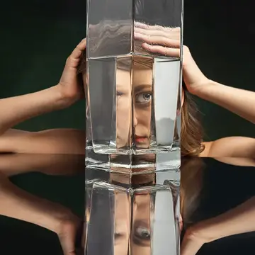 A woman on a black backgorund looking through a huge jug of water defoirming her features