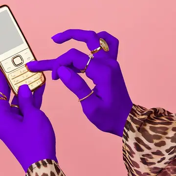 Hands of a woman in a lepard print shirt and with purple gloves, scrolling on a phone