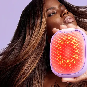 An African-American woman using a red light brush and flipping her fabulous, lush, smooth hair on a pink background