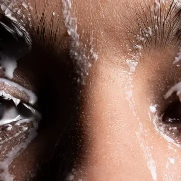 A closeup uf a womans eyes and a cleansing product dripping over her face