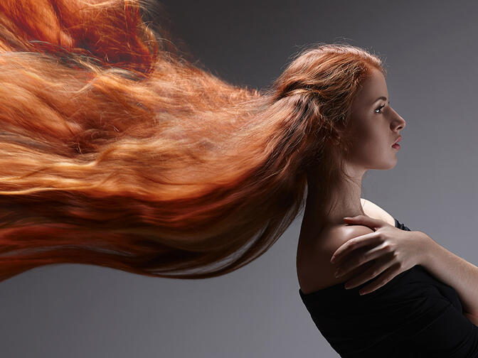 A beautiful young woman with very long ginger hair getting blown horizontally over to the left side of the screen
