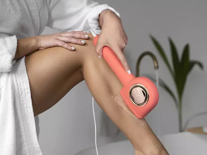 hair removal at home A woman with beautiful legs in white robe doing IPl hair removal at home in a beautiful space