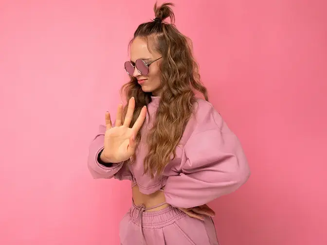 An attractive young woman on pink background with long hair in pink crop hoodie who has learned how to say no