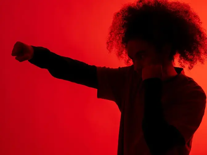 A shadow of a man with afro hair throwing a punch under red light