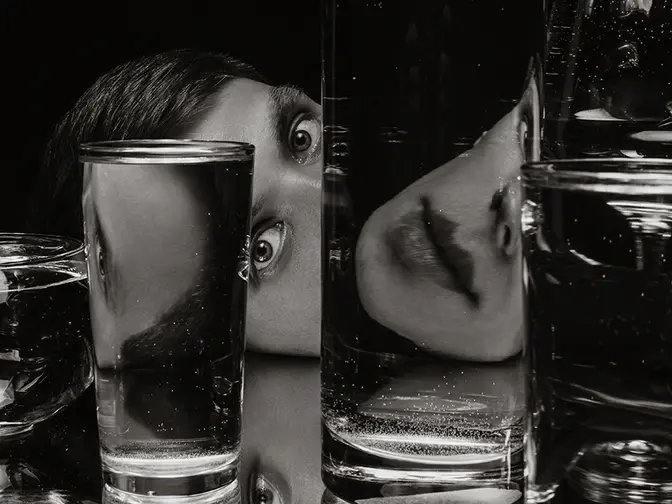 A person with interesting eyes with a face deconstructed by glasses of water in front of them
