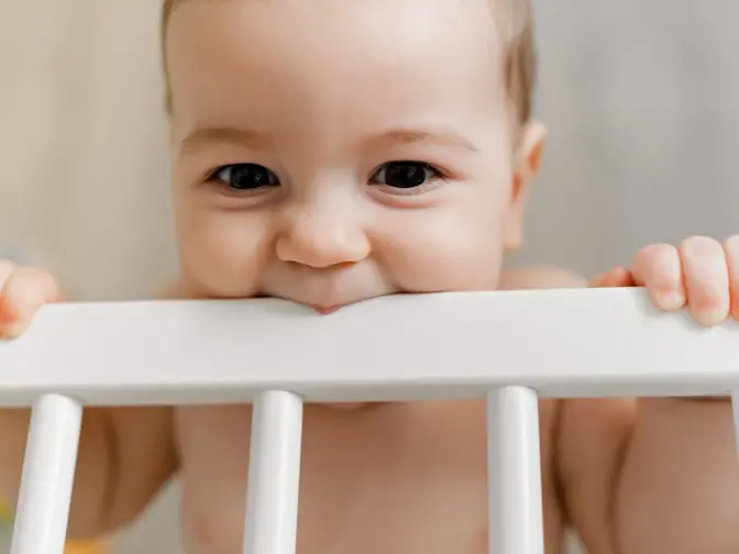 A cute teething baby chewing on the crib bar