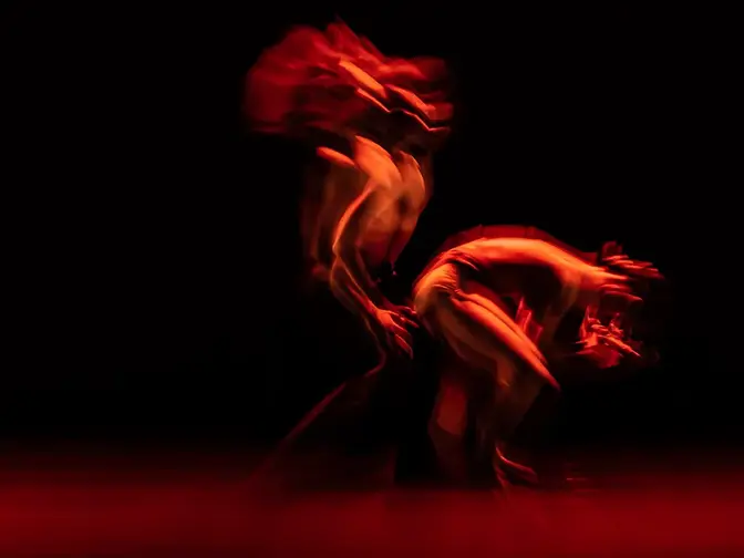 An abstract dance in a dark room with red lights representing the dualism and similarities of red light therapy vs infrared