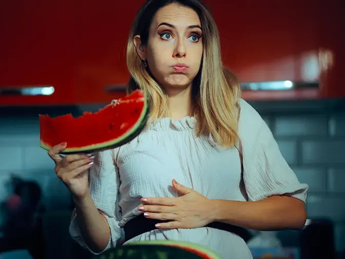 A bloated woman eating a watermellon  