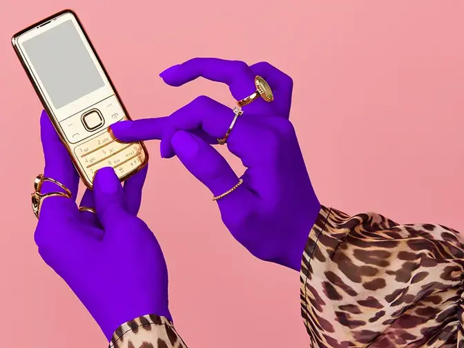 Hands of a woman in a lepard print shirt and with purple gloves, scrolling on a phone