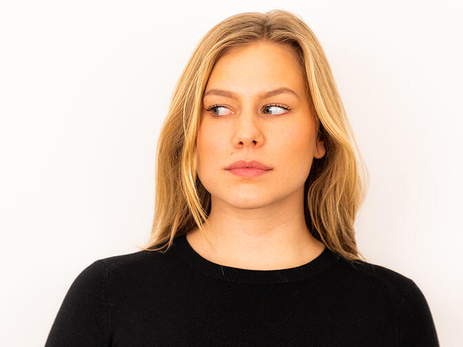 A young model with blonde hair, in a black jumper, looking to her right