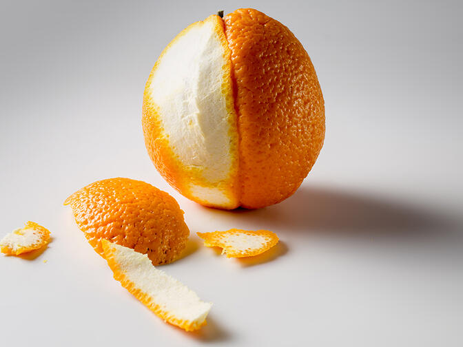 A photo of a half-peeled orange on a white surface