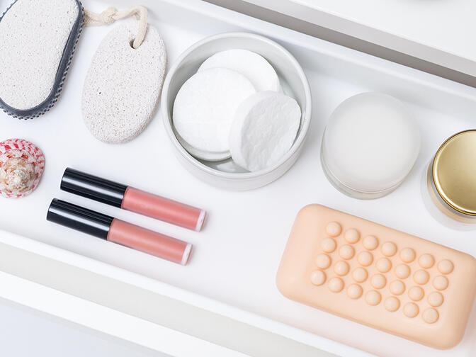 A cosmetic drawer with neatly organized soap, creams, cotton pads, pumice stone, pink lip gloss, and a sea shell