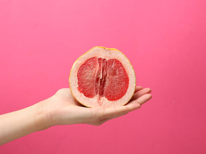 Female hand holding half of grapefruit on pink background