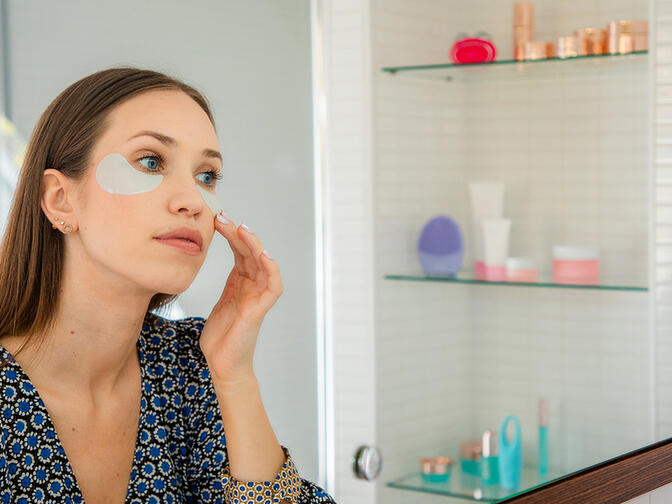 Young model with under-eye patches in a bathroom in front of a mirror