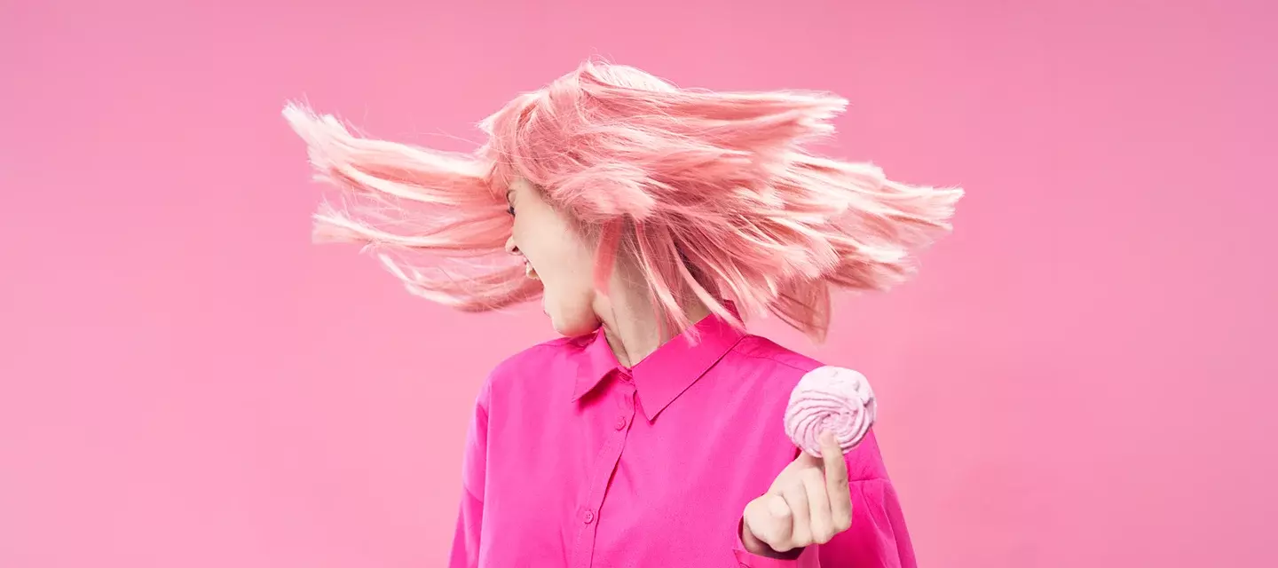 Sugar detox A silver blond-haired woman in pink, on a pink background holding a pink doughnut with hair flying in the air as she turns away from the pastry in her hand