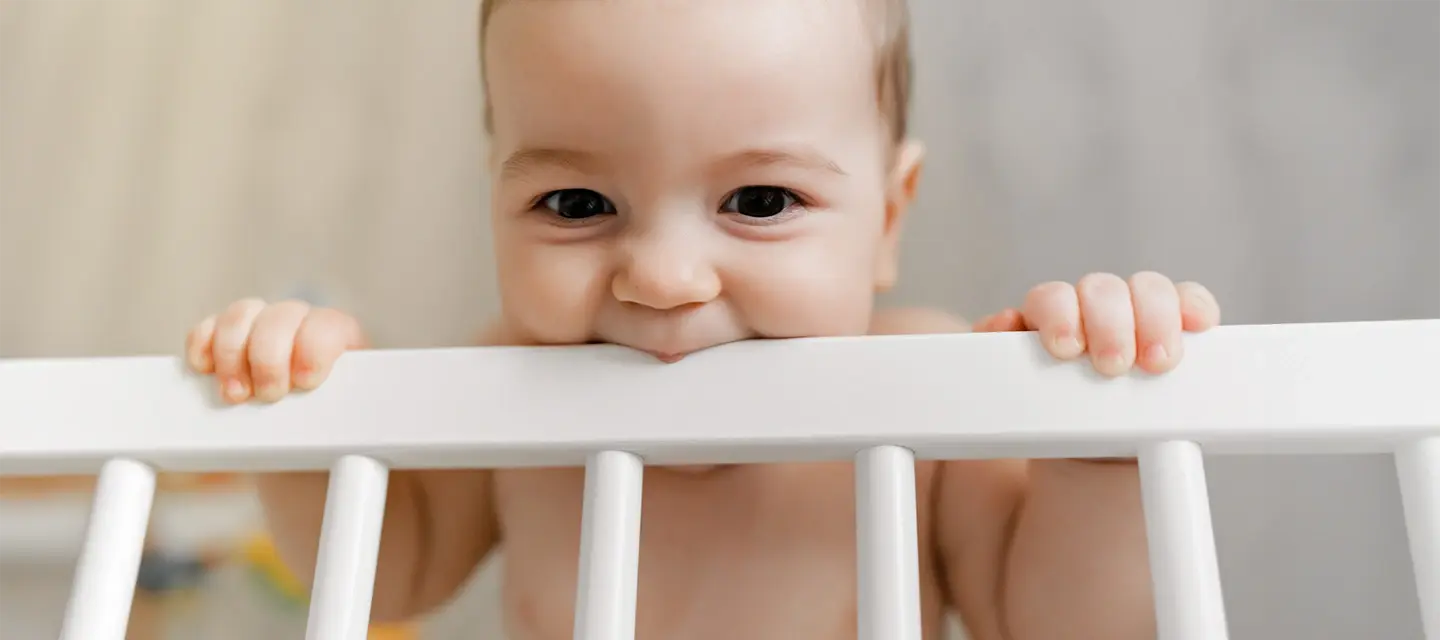 A cute teething baby chewing on the crib bar