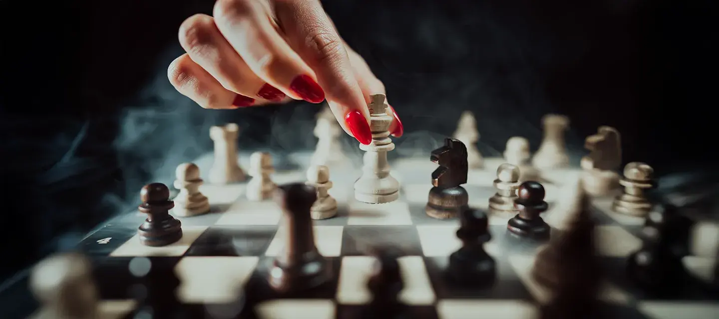 A female hand with red nail polish moving a chess figure on a dramatic dark backgorund with smokek