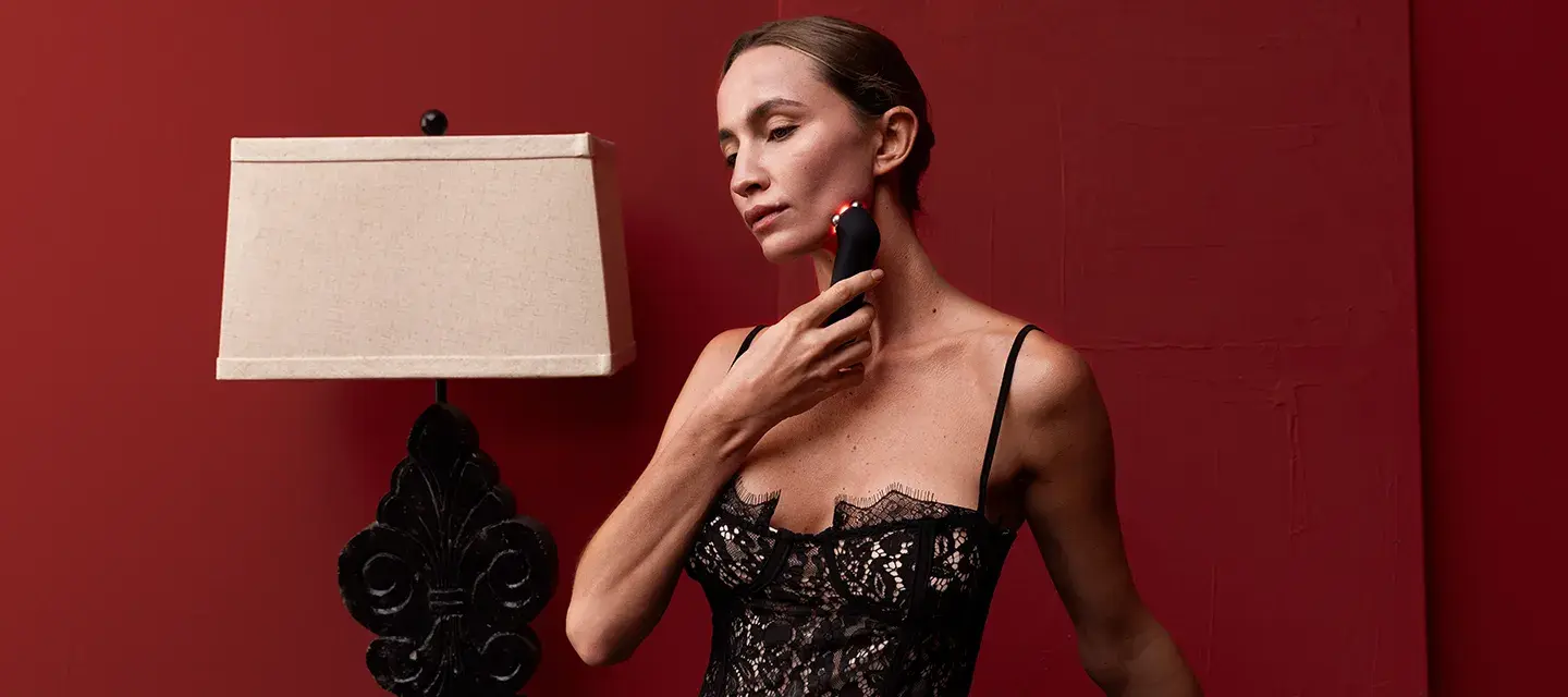 A beautiful woman in lingerie using FAQ 402 dual microcurrent device for skin tightening in a red room