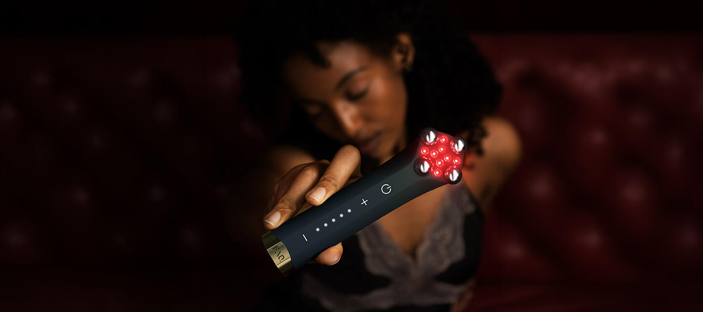 A blurry woman in the shadows holding FAQ 402 dual microcurrent and NIR facial toning device in a closeup main frame