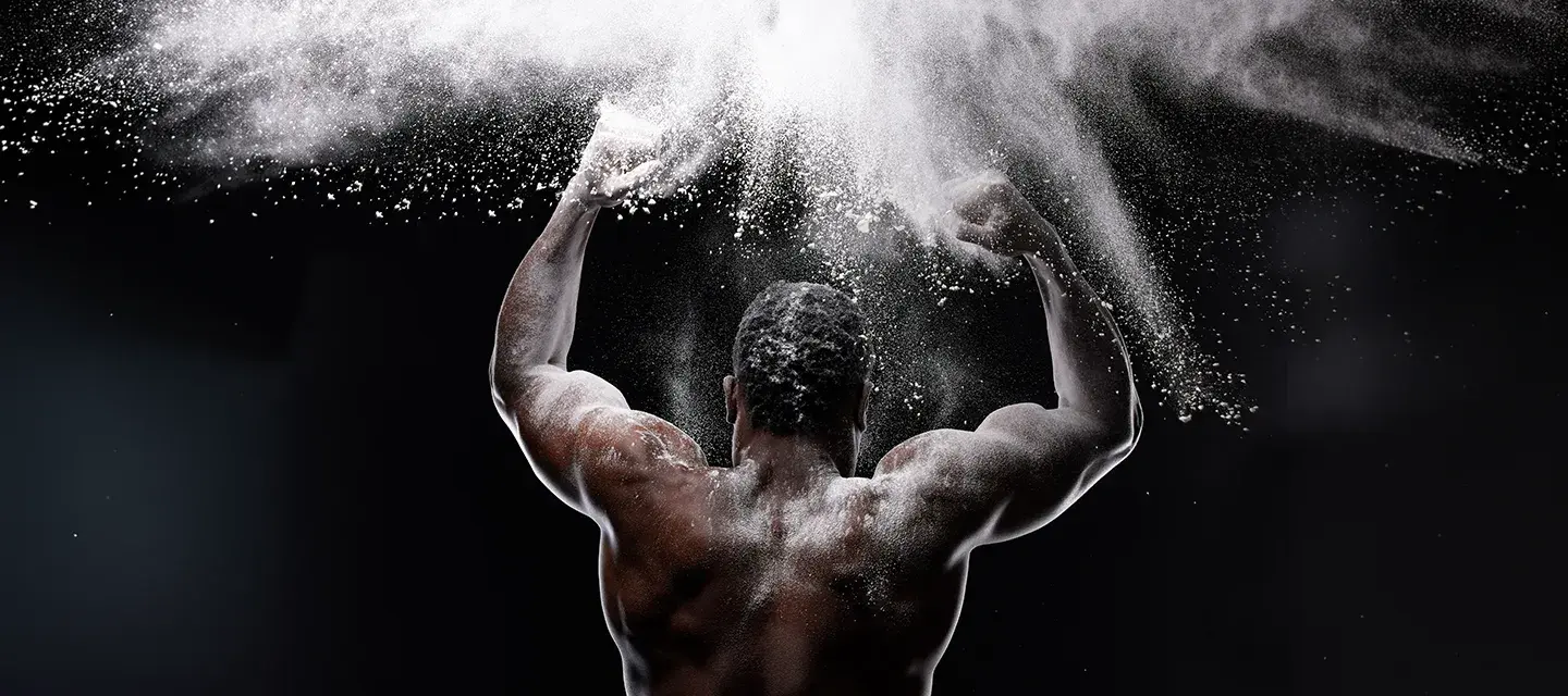 A muscular back of an African-American man clapping his hands covered in white powder in the air on a dark bacground