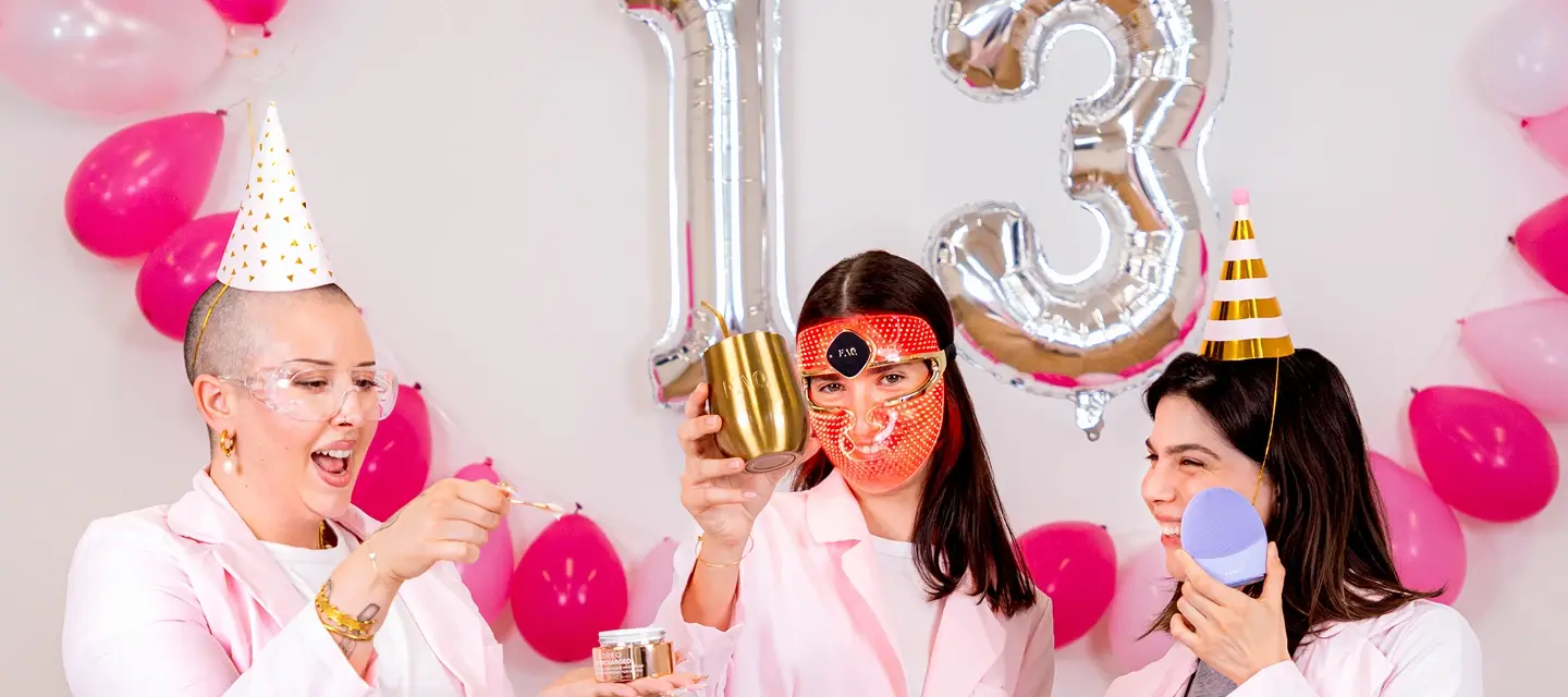 Three young women celebrating FOREO birthday sale with drinks and doing skincare in a white and pink setting