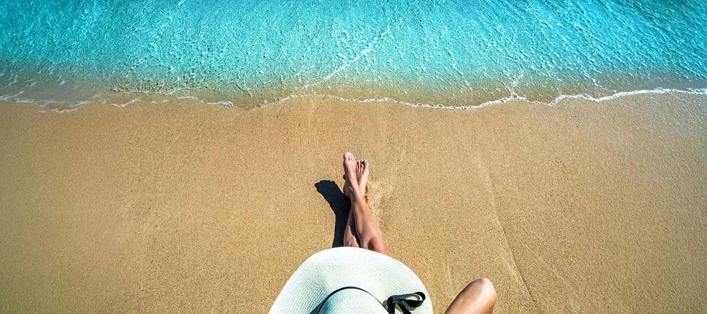 A woman in a white wide-brimmed hat sitting on a beautiful sandy beach