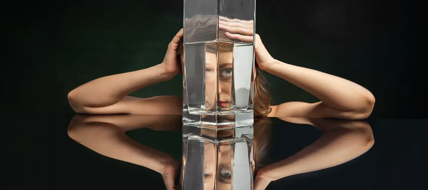 A woman on a black backgorund looking through a huge jug of water defoirming her features