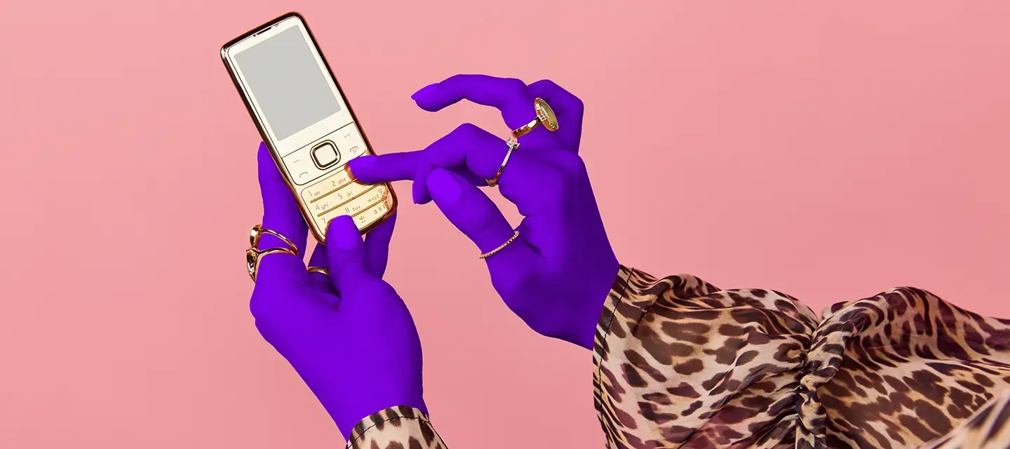 Hands of a woman in a lepard print shirt and with purple gloves, scrolling on a phone