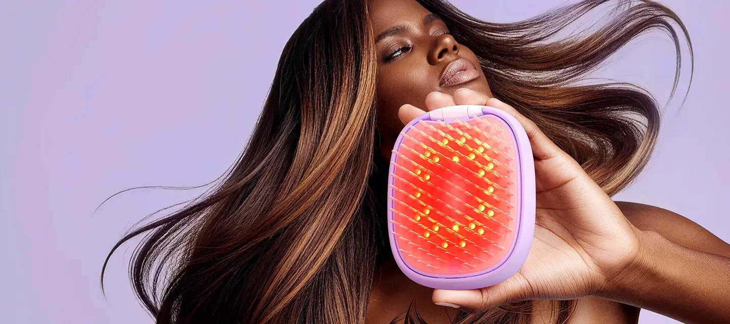 An African-American woman using a red light brush and flipping her fabulous, lush, smooth hair on a pink background