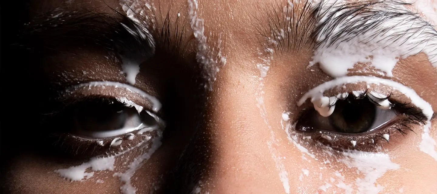 A closeup uf a womans eyes and a cleansing product dripping over her face