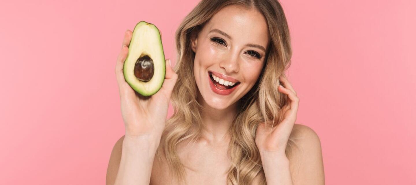 Las vitaminas y el cuidado facial están muy vinculados. Te contamos cuáles son las vitaminas que más influyen en el mantenimiento de la piel. Vitaminas y cuidado facial. Una mujer sostiene un aguacate.
