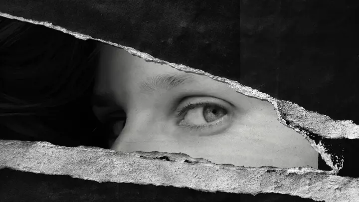 A torn up black and wihte poster on the wall where only a womans eyes remain, looking at the viewer