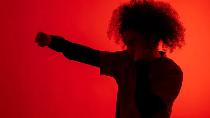 A shadow of a man with afro hair throwing a punch under red light