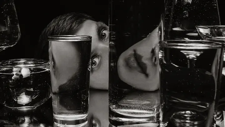 A person with interesting eyes with a face deconstructed by glasses of water in front of them